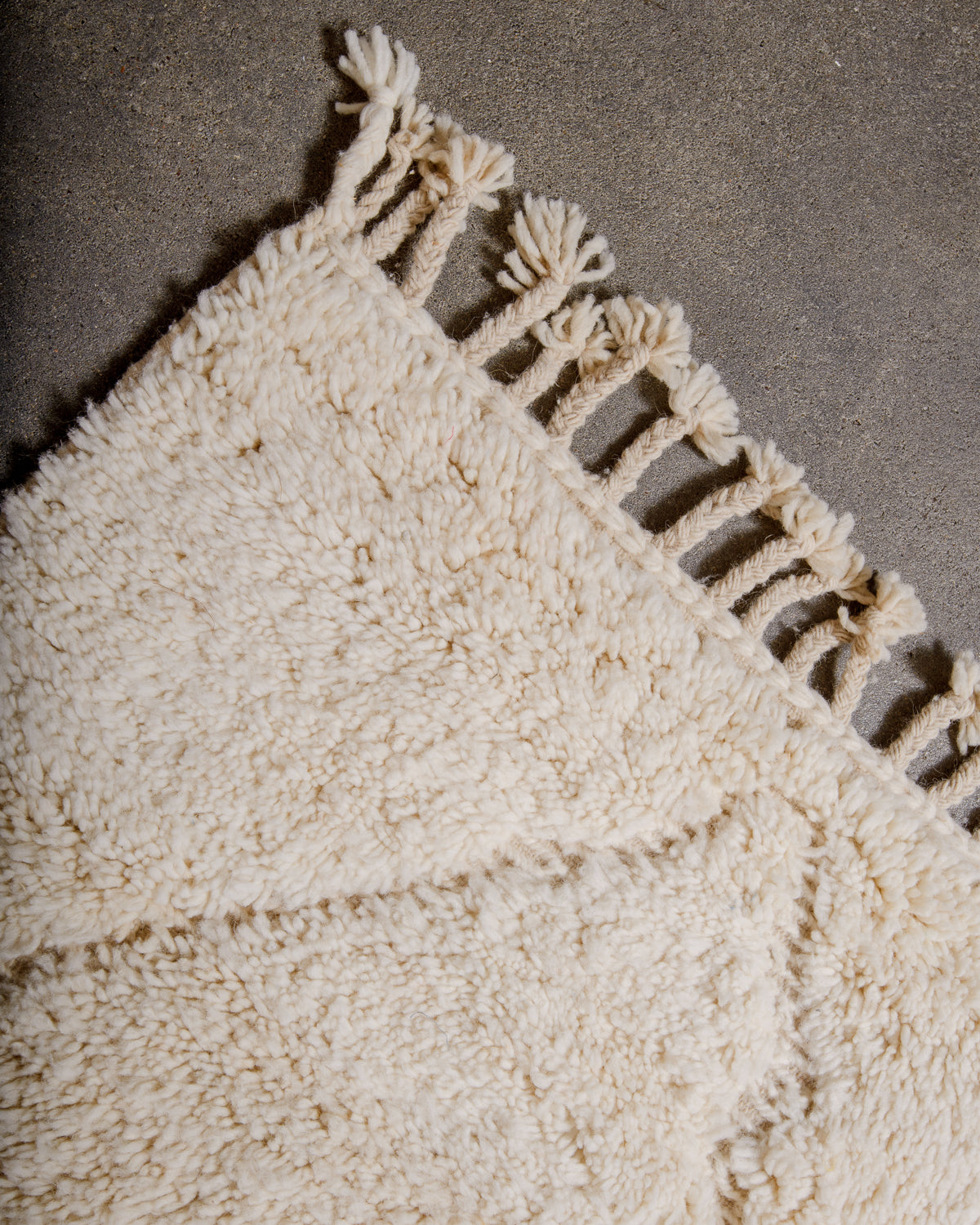 Corner of cream Beniourain rug with natural wool tassels.